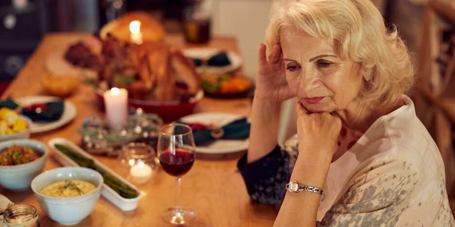 Senior woman feeling sad while sitting alone at dining table on Thanksgiving.